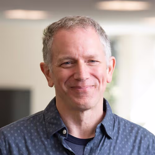Portrait of a smiling team member in a casual button-up, representing the human side of enterprise security