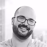 Smiling bald man with glasses and a beard in an outdoor setting.