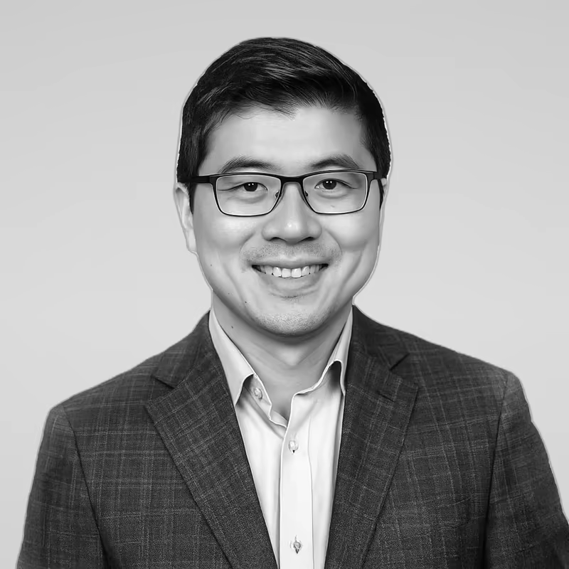 Black and white portrait of Jian Gong on a light gray studio background.