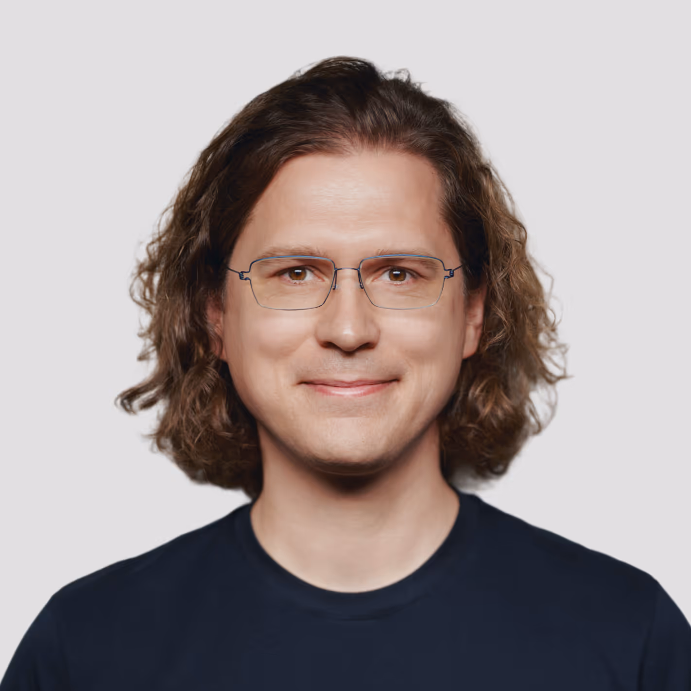 Smiling man with shoulder-length wavy brown hair and rectangular glasses wearing a black shirt.